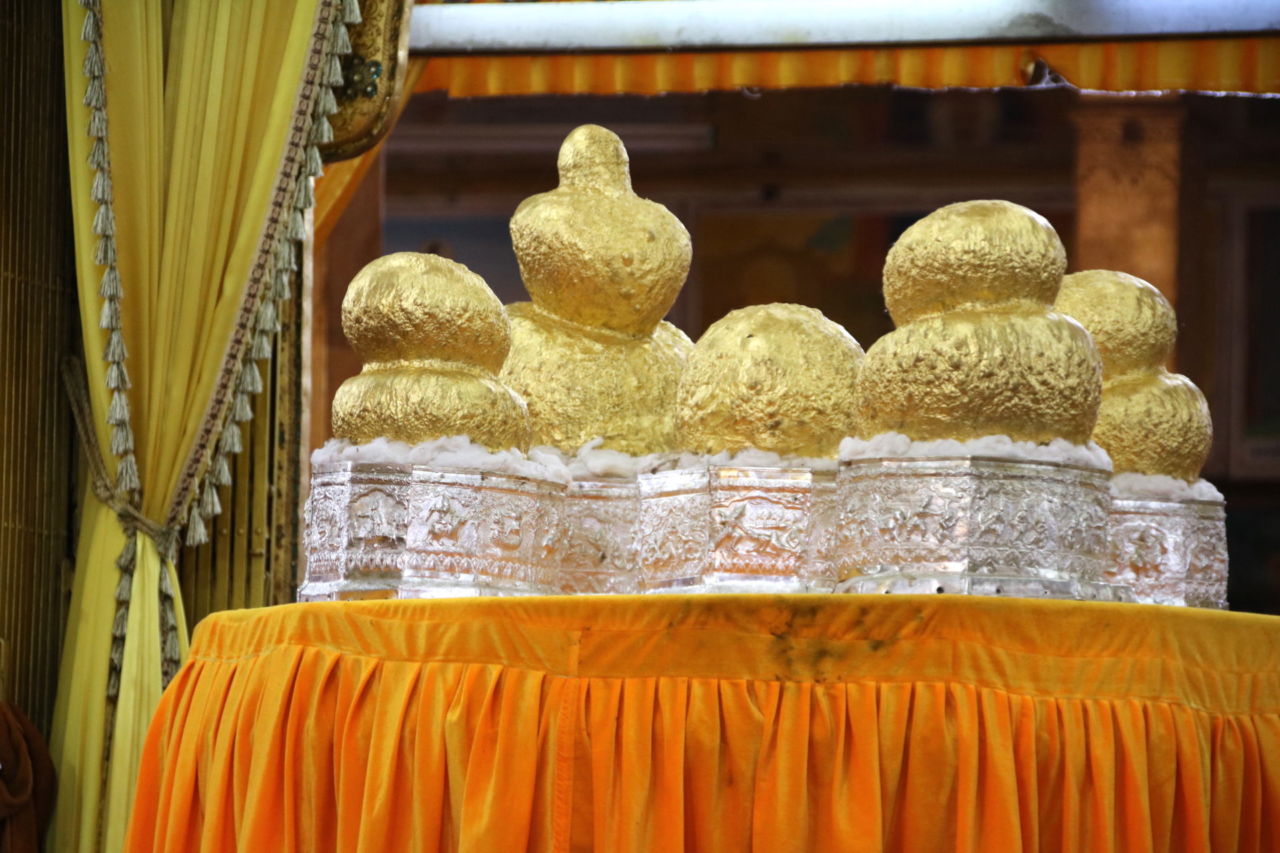 Buddhafiguren bis zur Unkenntlichkeit mit Goldplättchen verschönert Buddha Figuren aus Gold auf einem Tisch mit oranger Decke