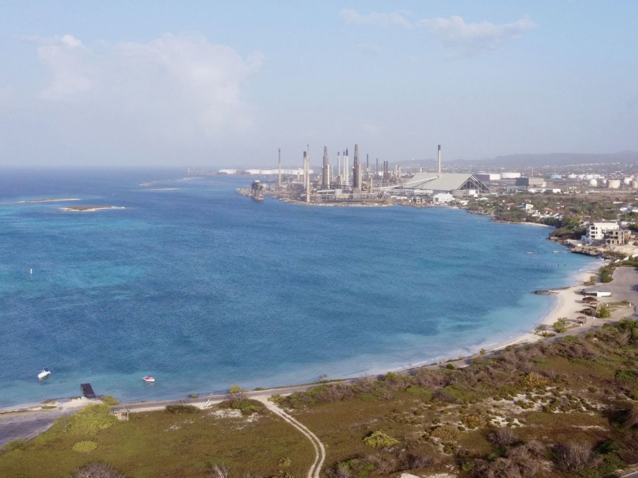 Eine Luftaufnahme eines Strandes mit Strand im Vordergrund und einer Fabrik im Hintergrund
